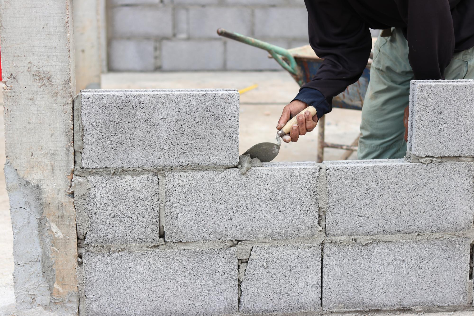 Masonry contractor applying mortar to brick wall during construction – Retaining Solutions